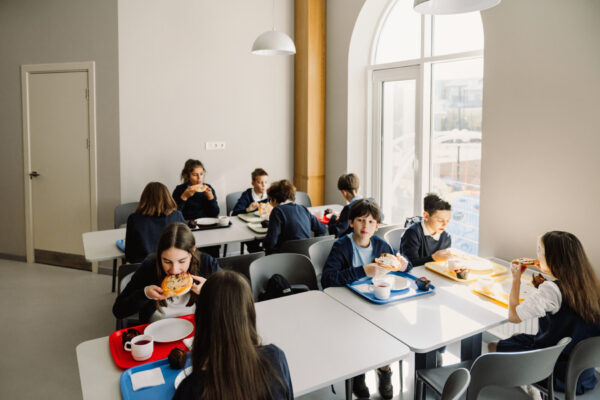 Group of primary school kids wearing uniform eating at table in school cafeteria