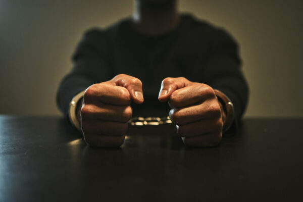 Interrogation, jail and hands of criminal in handcuffs for interview, investigation and arrested in station. Security, law and closeup of man, burglar or thief for crime, stealing and theft in prison.